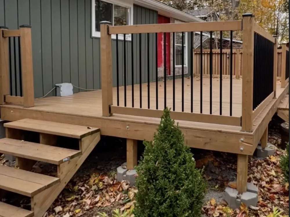 Deck stairs and railing against a dark green board-and-batten house in autumn