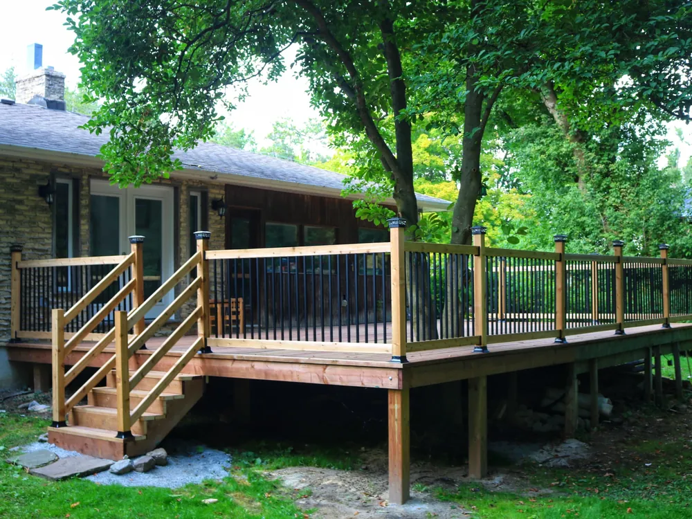 Pressure-treated deck with black aluminum pickets wrapped around a stone bungalow