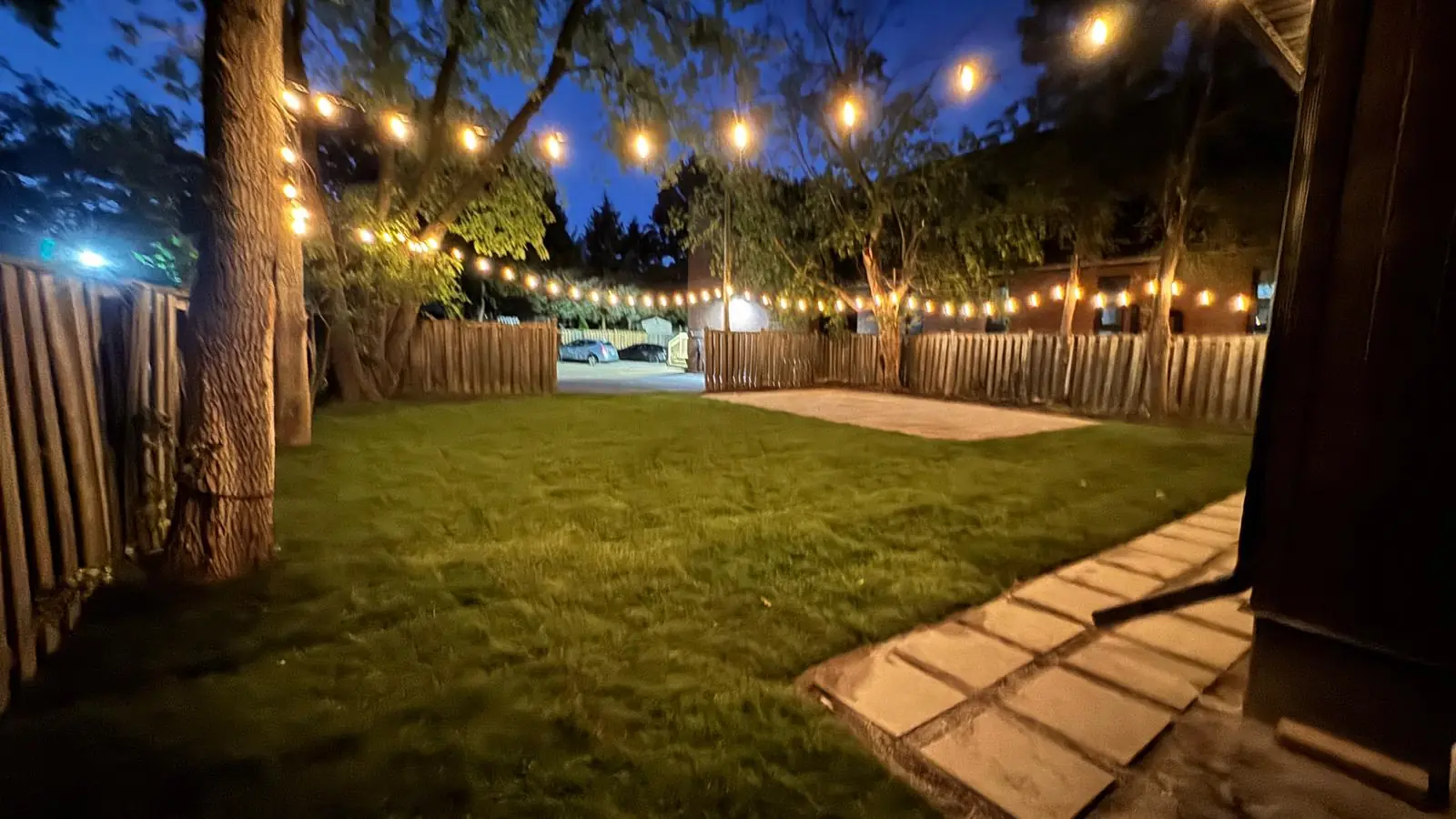 Finished backyard at dusk with string lights over a slab patio and new lawn