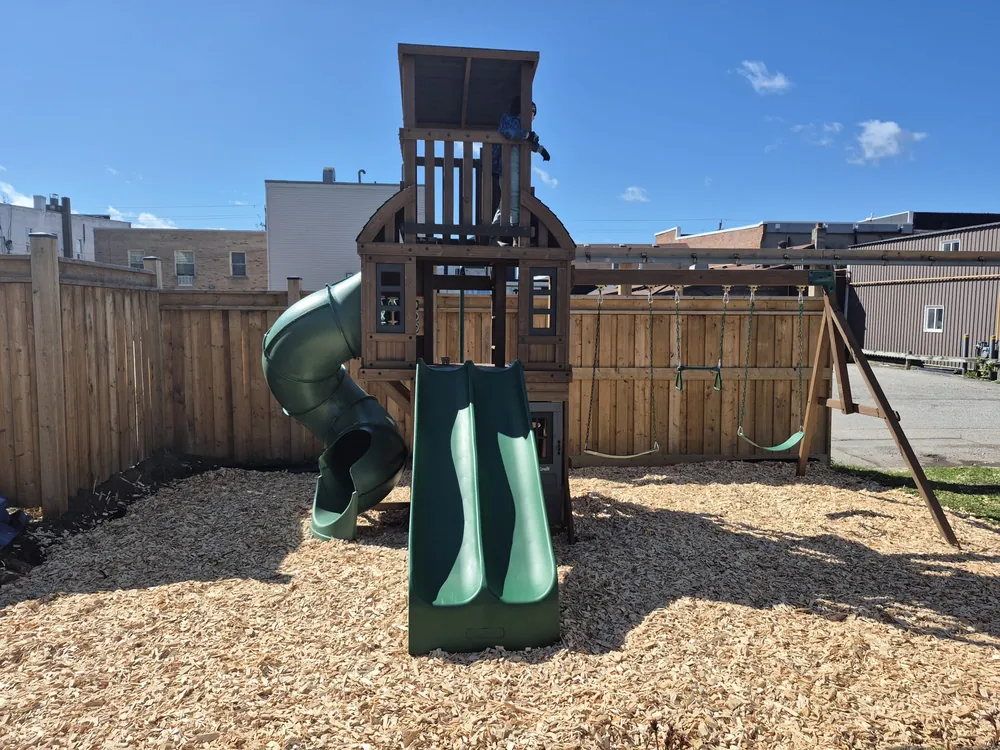 Play structure with slides and swings on a fresh woodchip base inside a new board fence